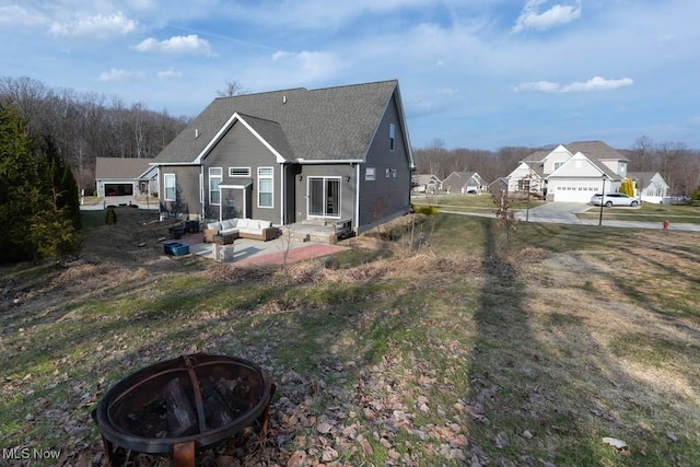 rear view of property with an outdoor living space with a fire pit, roof with shingles, a patio area, and a residential view
