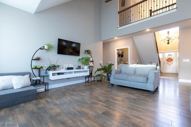 living area featuring wood finished floors, a chandelier, a high ceiling, baseboards, and ceiling fan