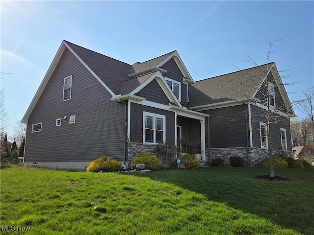 view of home's exterior featuring a lawn, stone siding, and a shingled roof