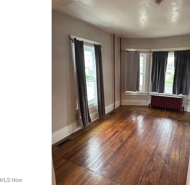empty room featuring radiator heating unit, a wealth of natural light, hardwood / wood-style floors, and baseboards