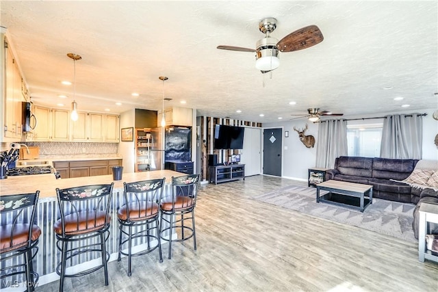 kitchen featuring light countertops, a peninsula, ceiling fan, stainless steel microwave, and light wood-type flooring