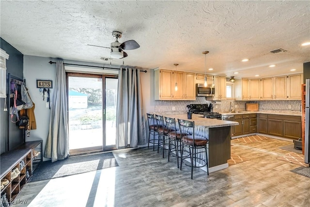 kitchen featuring a ceiling fan, a kitchen bar, a peninsula, stainless steel microwave, and range with gas stovetop