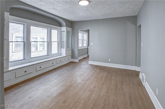 empty room featuring light wood finished floors, baseboards, visible vents, and a textured ceiling