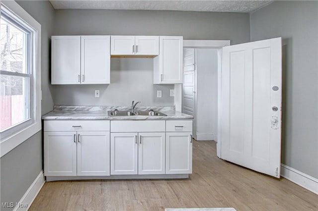 kitchen featuring white cabinetry, light countertops, a sink, and light wood finished floors