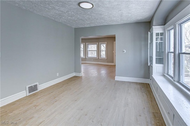 unfurnished room featuring wood finished floors, a textured ceiling, baseboards, and visible vents