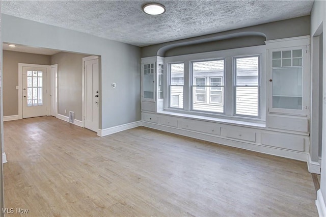 empty room featuring baseboards, a textured ceiling, visible vents, and light wood-type flooring