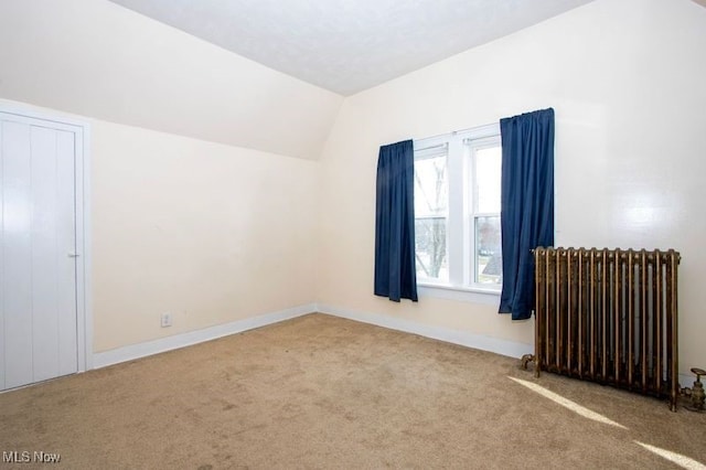empty room with baseboards, carpet flooring, vaulted ceiling, and radiator