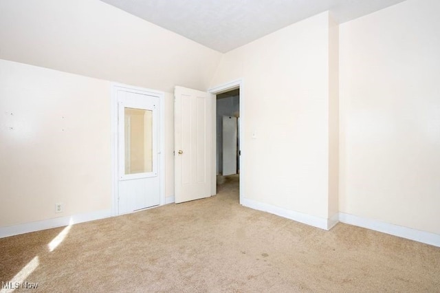 spare room featuring baseboards, lofted ceiling, and light carpet