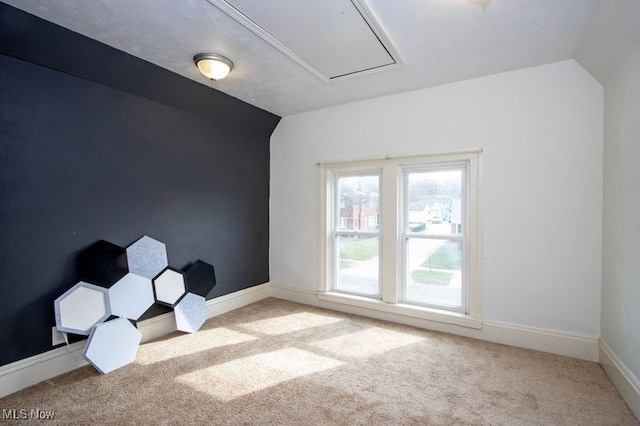 unfurnished room featuring attic access, baseboards, vaulted ceiling, and carpet