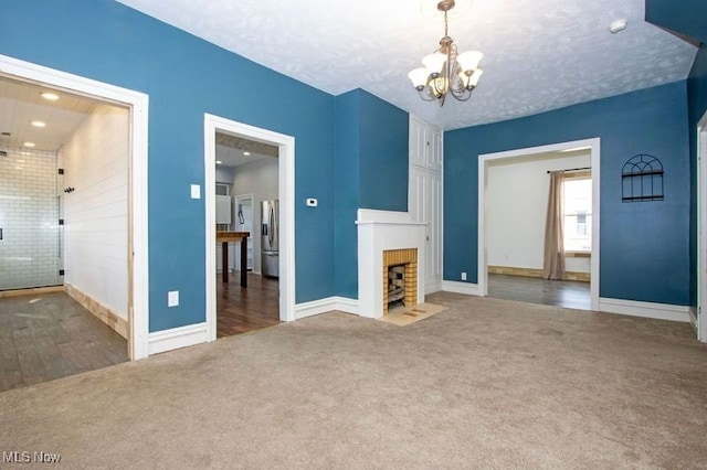 unfurnished living room with a fireplace with flush hearth, a notable chandelier, carpet, and a textured ceiling