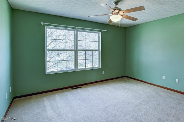 carpeted spare room featuring ceiling fan, baseboards, a textured ceiling, and visible vents