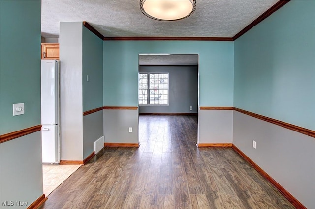 unfurnished room featuring a textured ceiling, wood finished floors, baseboards, and visible vents