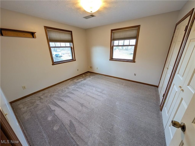 unfurnished bedroom featuring multiple windows, visible vents, baseboards, and a textured ceiling