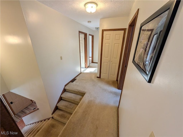 hall featuring stairs, baseboards, light colored carpet, and a textured ceiling