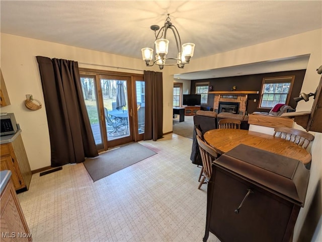 dining space featuring baseboards, visible vents, a glass covered fireplace, and an inviting chandelier