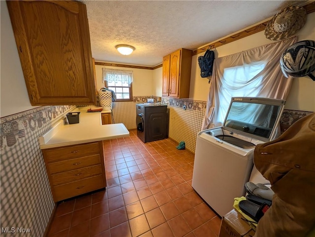 kitchen with a textured ceiling, dark tile patterned floors, washer / clothes dryer, brown cabinetry, and wainscoting