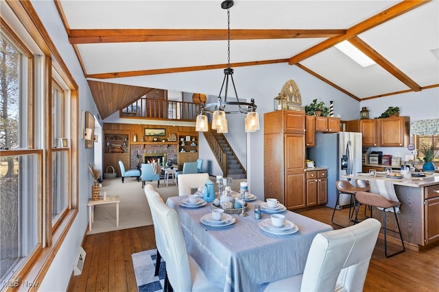 1122 Lake Rd, Conneaut, OH 44030 - dining room with stairs, a fireplace, wood finished floors, vaulted ceiling with beams, and a notable chandelier