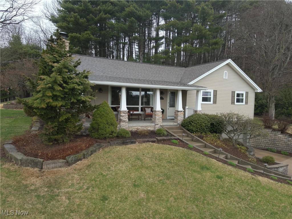 view of front of home with covered porch, a front yard, a shingled roof, and a chimney