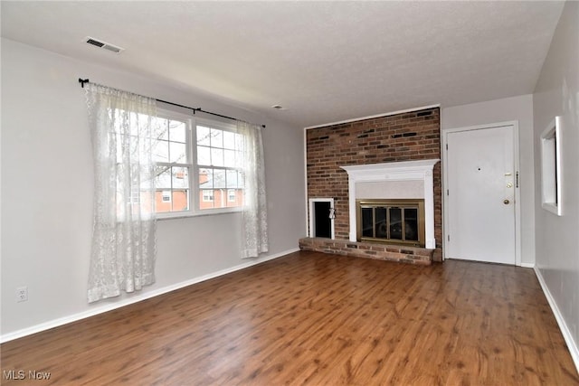 unfurnished living room featuring baseboards, visible vents, wood finished floors, and a fireplace