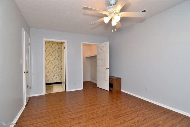 unfurnished bedroom featuring a closet, baseboards, connected bathroom, wood finished floors, and a walk in closet