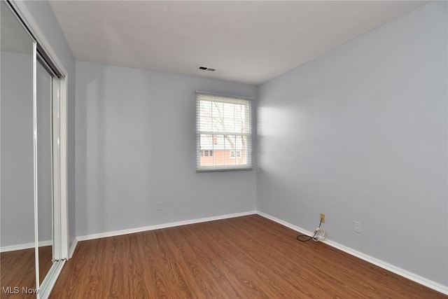 unfurnished bedroom with dark wood finished floors, baseboards, visible vents, and a closet
