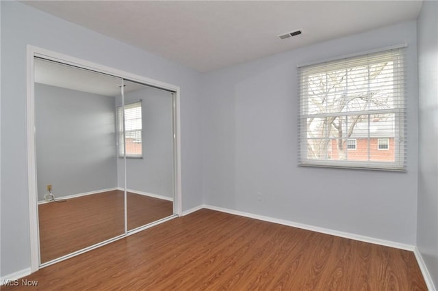 unfurnished bedroom featuring wood finished floors, baseboards, a closet, and visible vents