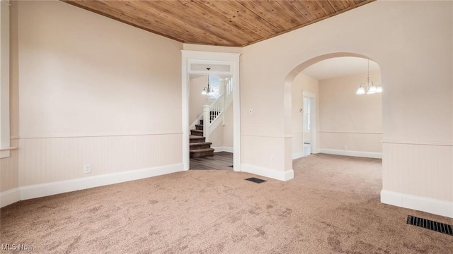 empty room featuring carpet, a wainscoted wall, wood ceiling, arched walkways, and visible vents