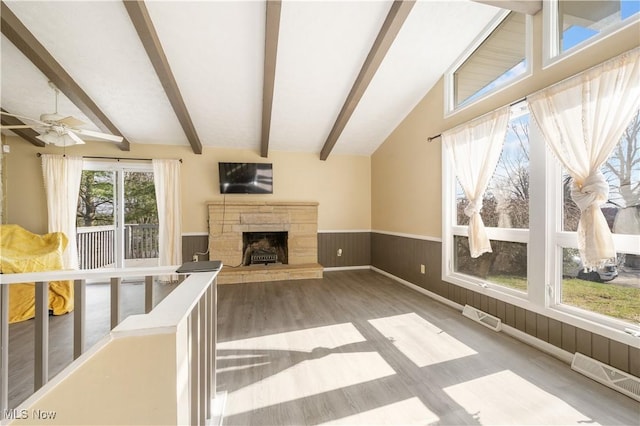 70 Iroquois Trl, Malvern, OH 44644 - unfurnished living room featuring visible vents, ceiling fan, a stone fireplace, vaulted ceiling with beams, and wainscoting