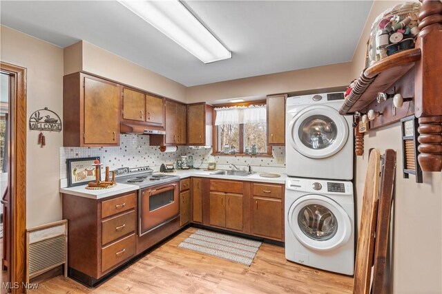 kitchen with light countertops, under cabinet range hood, electric stove, stacked washer and dryer, and brown cabinetry