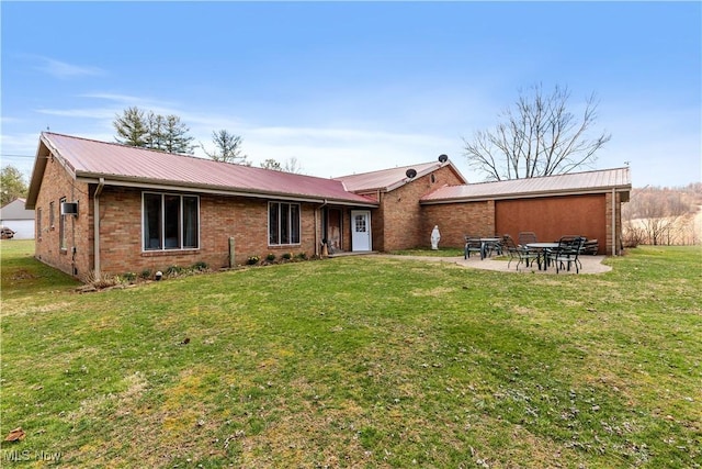 back of property with a yard, brick siding, a patio area, and metal roof