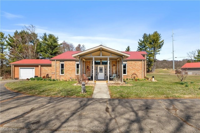 view of front of house featuring a front yard, brick siding, aphalt driveway, metal roof, and a garage