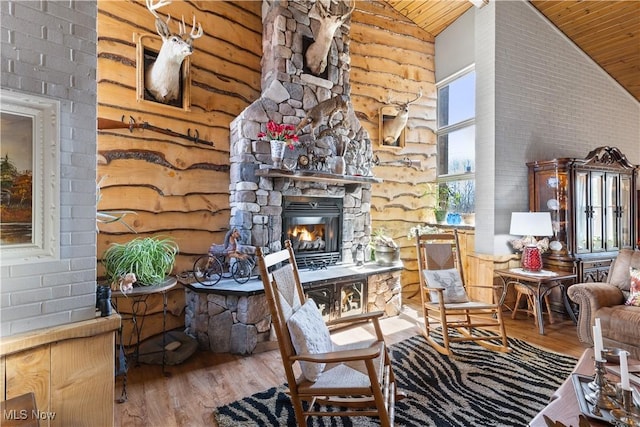 living room with wooden ceiling, high vaulted ceiling, a stone fireplace, and wood finished floors