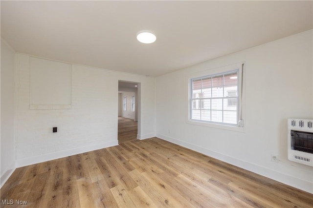 spare room featuring baseboards, heating unit, and light wood finished floors