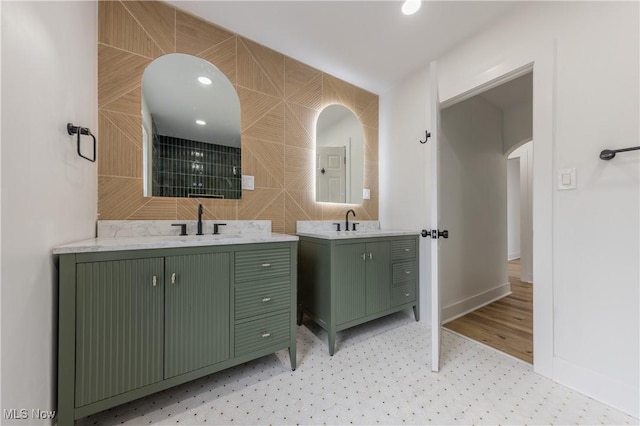 full bathroom with a sink, two vanities, baseboards, and tile walls