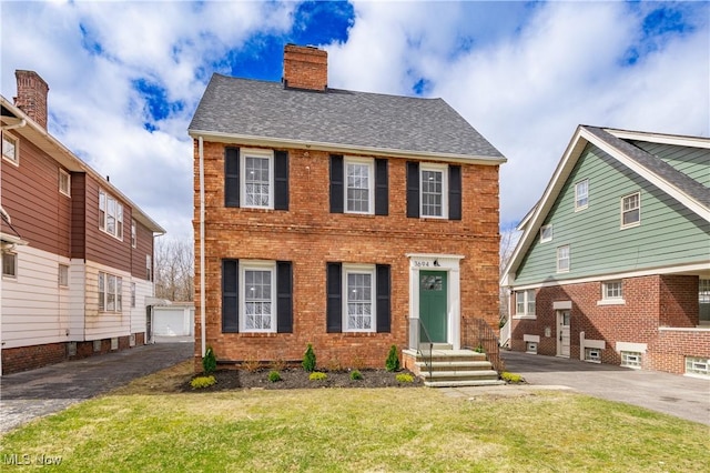 view of front of home featuring brick siding, driveway, a front lawn, and a chimney