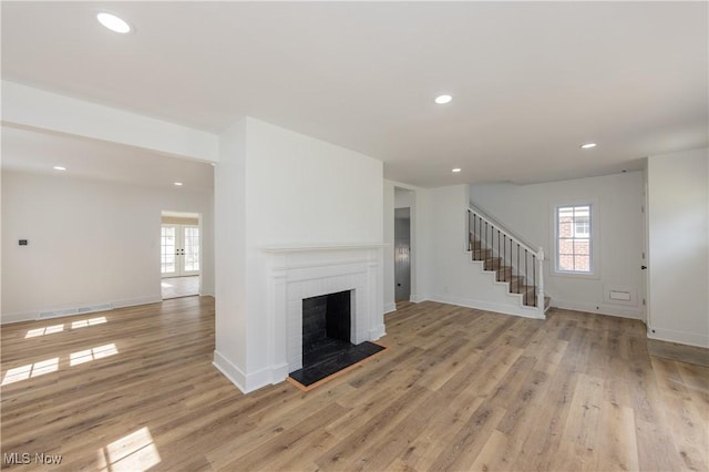 unfurnished living room featuring light wood-type flooring, stairway, recessed lighting, and a healthy amount of sunlight