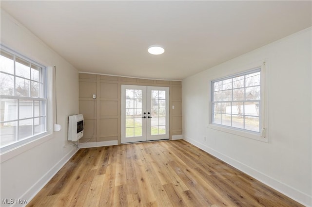interior space with a healthy amount of sunlight, heating unit, french doors, and light wood finished floors