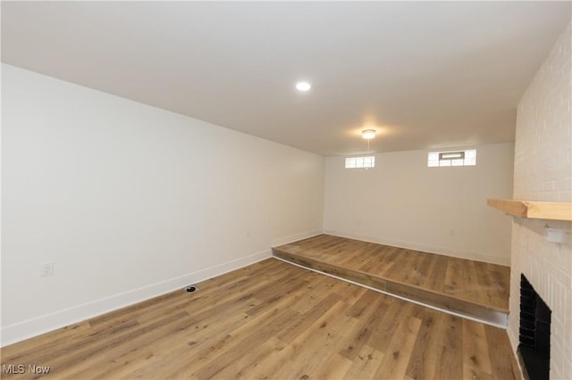 basement with baseboards, light wood-type flooring, and a brick fireplace