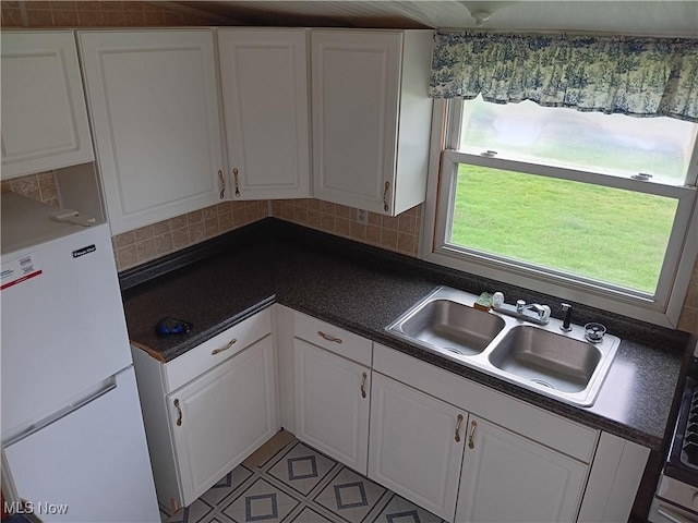 kitchen featuring a sink, freestanding refrigerator, white cabinetry, dark countertops, and decorative backsplash