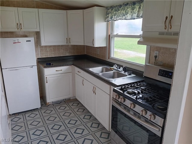 kitchen with stainless steel range with gas stovetop, under cabinet range hood, a sink, freestanding refrigerator, and white cabinets
