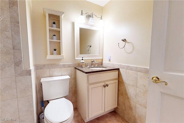 bathroom featuring toilet, a wainscoted wall, tile walls, and vanity