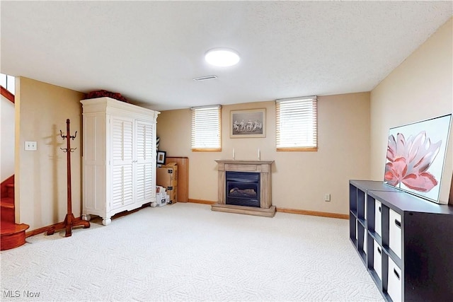 living room with carpet, baseboards, a textured ceiling, visible vents, and a glass covered fireplace