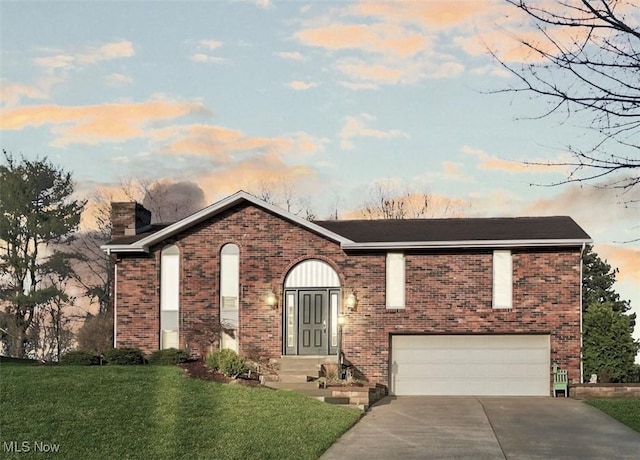 view of front facade with concrete driveway, a chimney, brick siding, a garage, and a yard