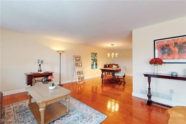 living room with a notable chandelier, visible vents, wood finished floors, and a textured ceiling