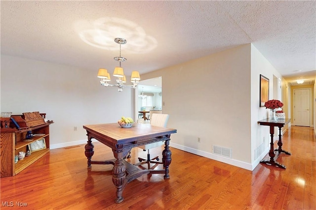 dining space featuring a notable chandelier, light wood finished floors, a textured ceiling, baseboards, and visible vents