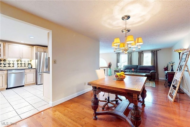 dining space with light wood finished floors, baseboards, a textured ceiling, and a chandelier