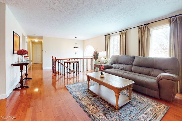 living room with baseboards, visible vents, light wood-style floors, and a textured ceiling