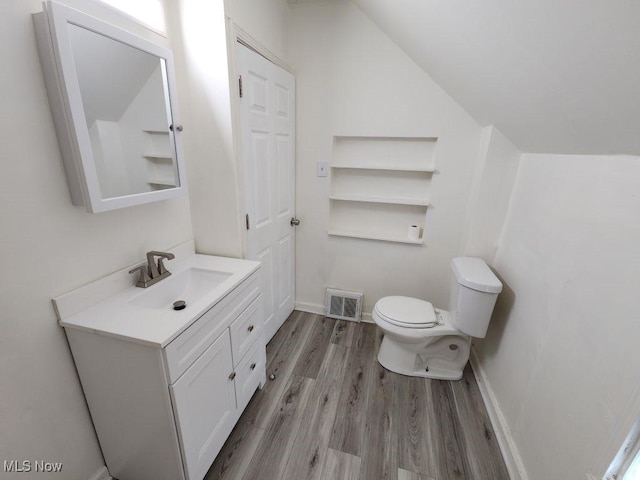 half bath featuring visible vents, toilet, vanity, vaulted ceiling, and wood finished floors