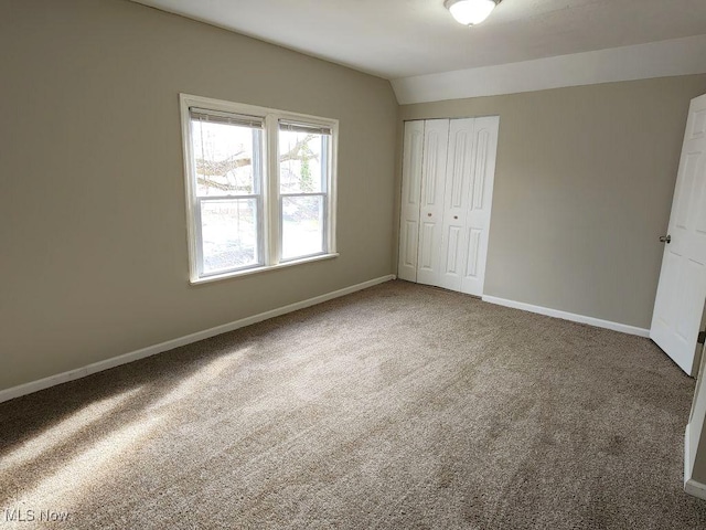 unfurnished bedroom featuring a closet, lofted ceiling, baseboards, and carpet floors