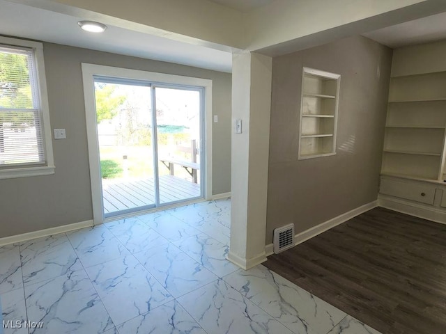 empty room with marble finish floor, visible vents, baseboards, and built in features